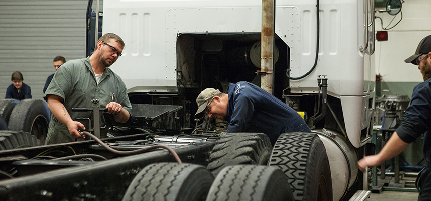 Three technicians work on a semi truck in a workshop